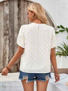 Woman wearing a white blouse with yellow polka dots and denim shorts outdoors.