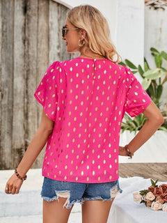 Woman wearing a pink polka dot top and denim shorts outdoors.