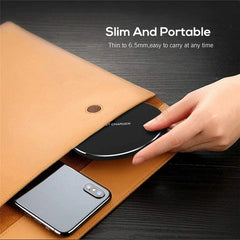 Hand holding a black wireless charger over a brown leather pouch with a phone inside, on a dark surface.