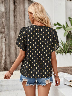 Woman wearing a black polka dot blouse and denim shorts outdoors.