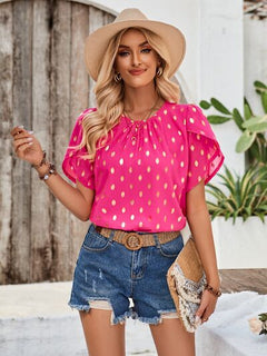 Woman wearing a pink polka dot blouse, denim shorts, and a straw hat outdoors.