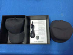 Black cap in an open box with a cable and paper on a blue surface
