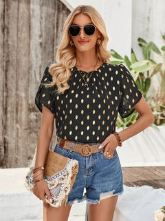 Woman wearing a black polka dot top and denim shorts outdoors.