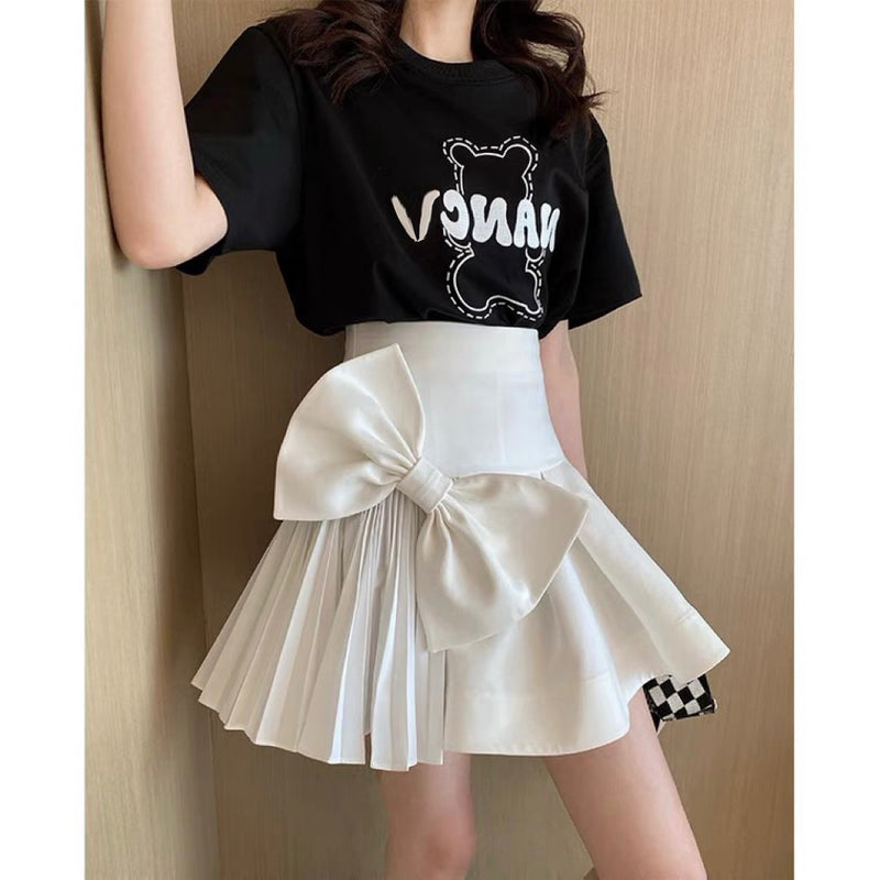 Person wearing a black crop top with white graphics and a white pleated skirt with a large bow.