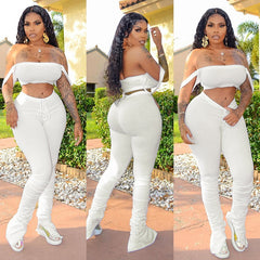 Woman in a white outfit posing outdoors with greenery in the background