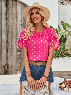 Woman wearing a pink polka dot blouse and denim shorts, standing outdoors.